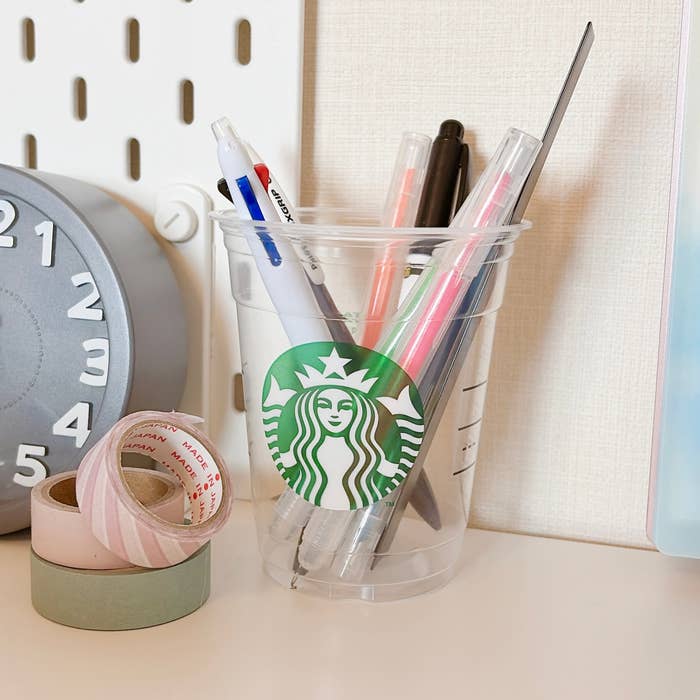 スターバックスのカップに収められたペンや文具類が、時計とマスキングテープのそばに置かれている。