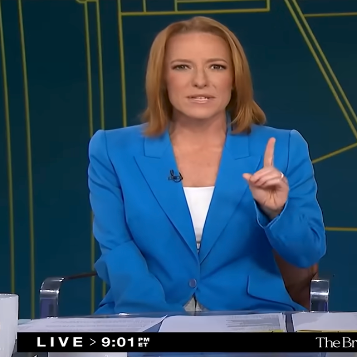 A speaker in a blue blazer gestures during a live broadcast, appearing knowledgeable and engaging with the audience