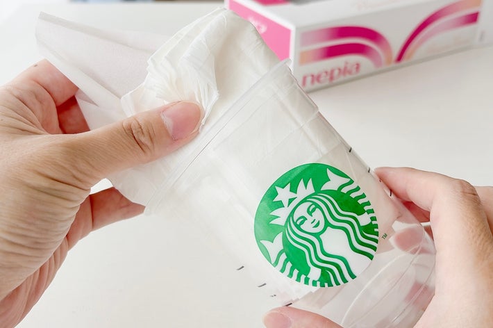 透明なスターバックスのカップにティッシュペーパーを入れて持っている手。背景にティッシュの箱が見える。