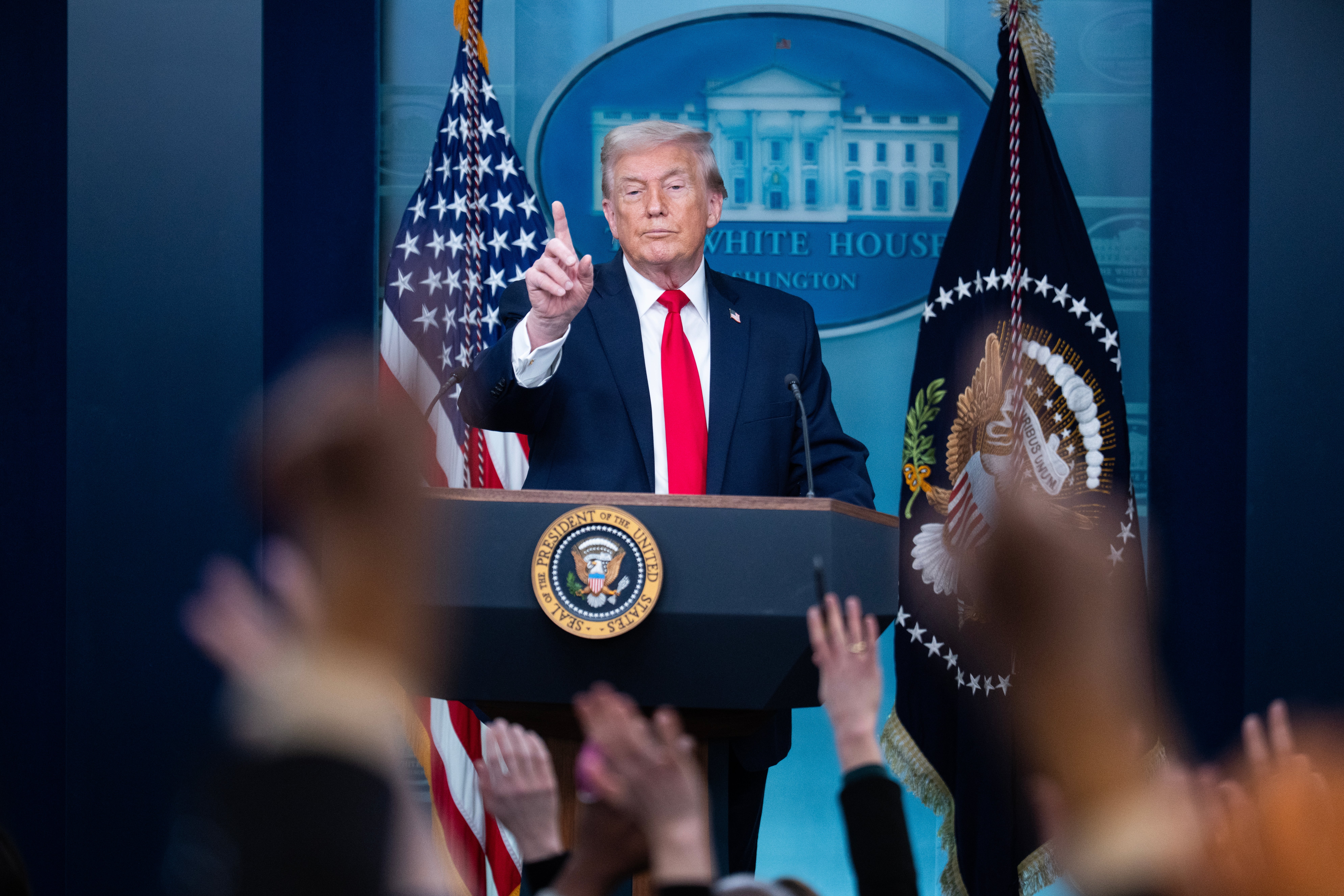 A nationalist fig astatine a podium successful a property briefing room, gestures to the audience. The U.S. emblem and the statesmanlike seal are disposable successful the background