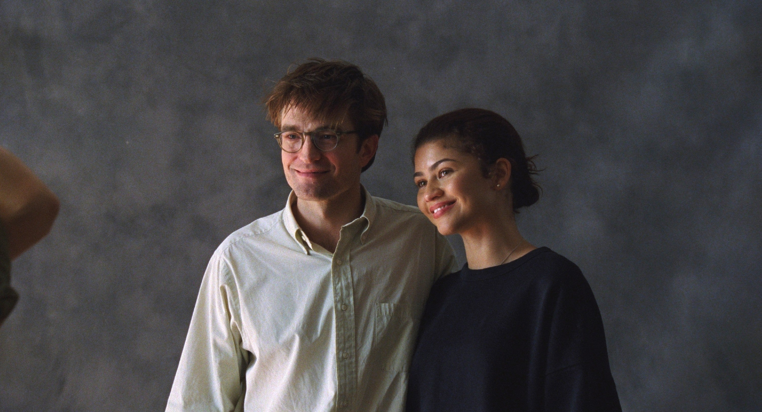 Two people posing together, smiling. The person on the left wears glasses and a button-up shirt; the person on the right wears a casual top