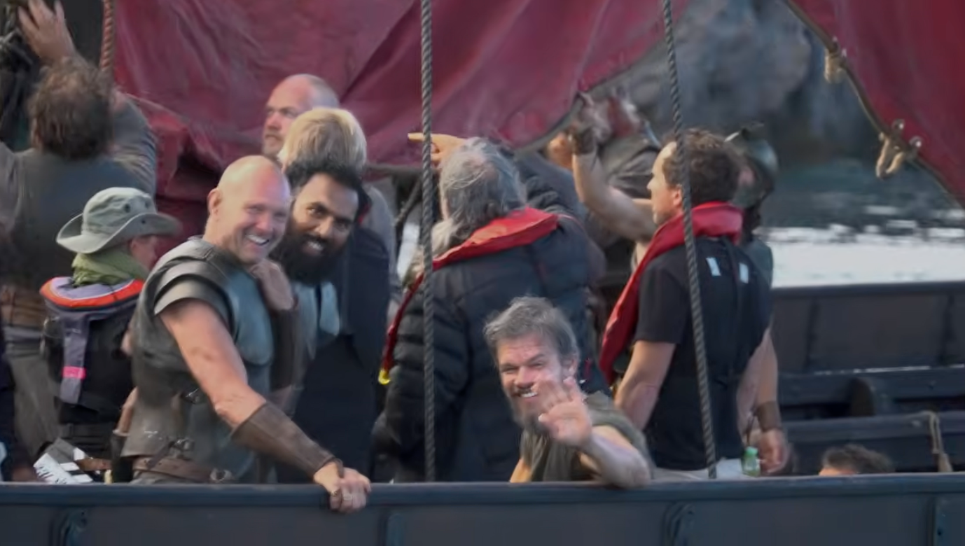 Group of people on a boat set, wearing costumes and winter jackets, smiling and waving