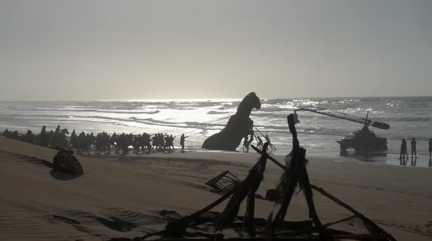 Film crew shooting near a shipwrecked giant statue on a desolate beach