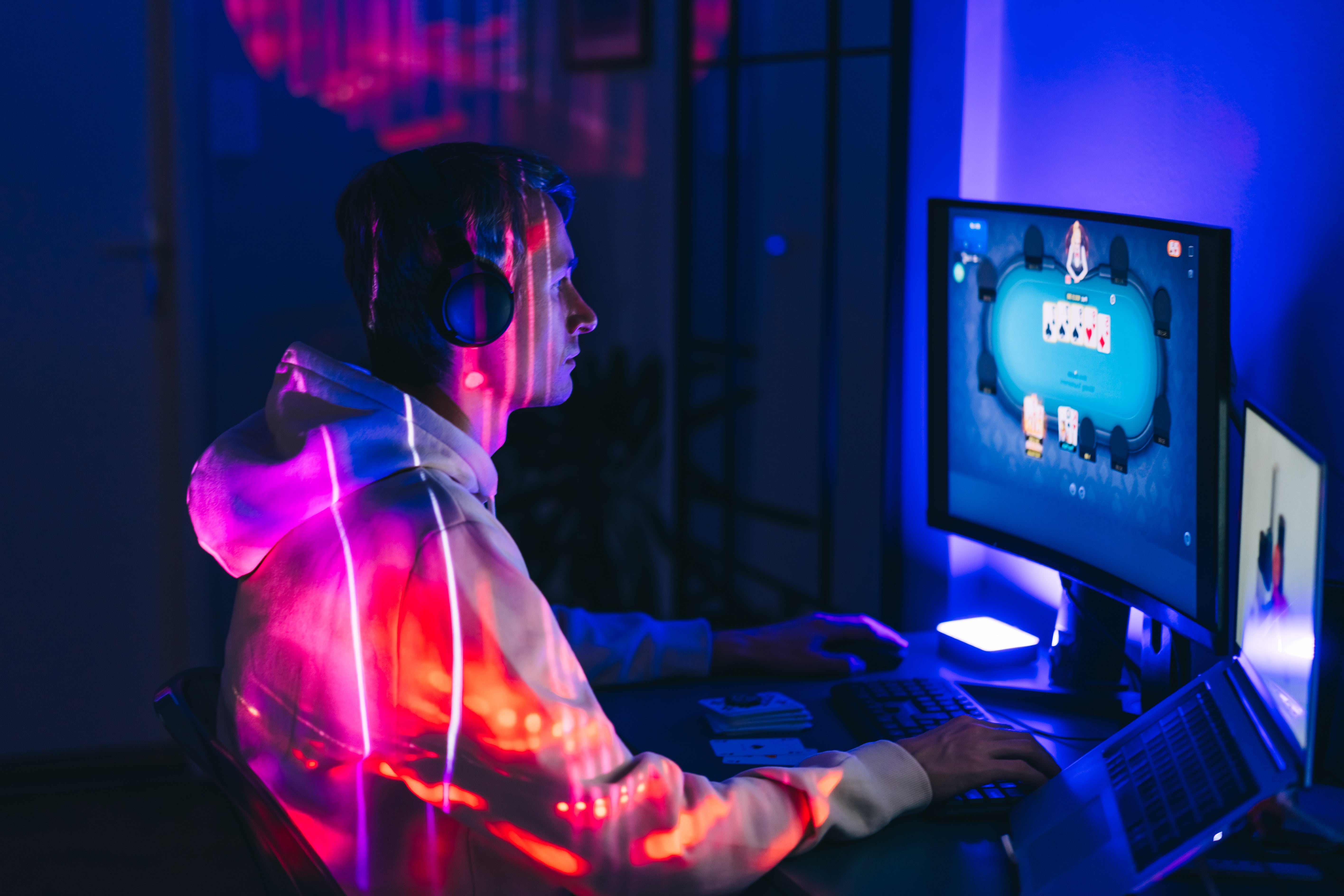 Person gaming connected a computer, wearing headphones and a hoodie. Colorful lights illuminate the room, reflecting excitement and focus