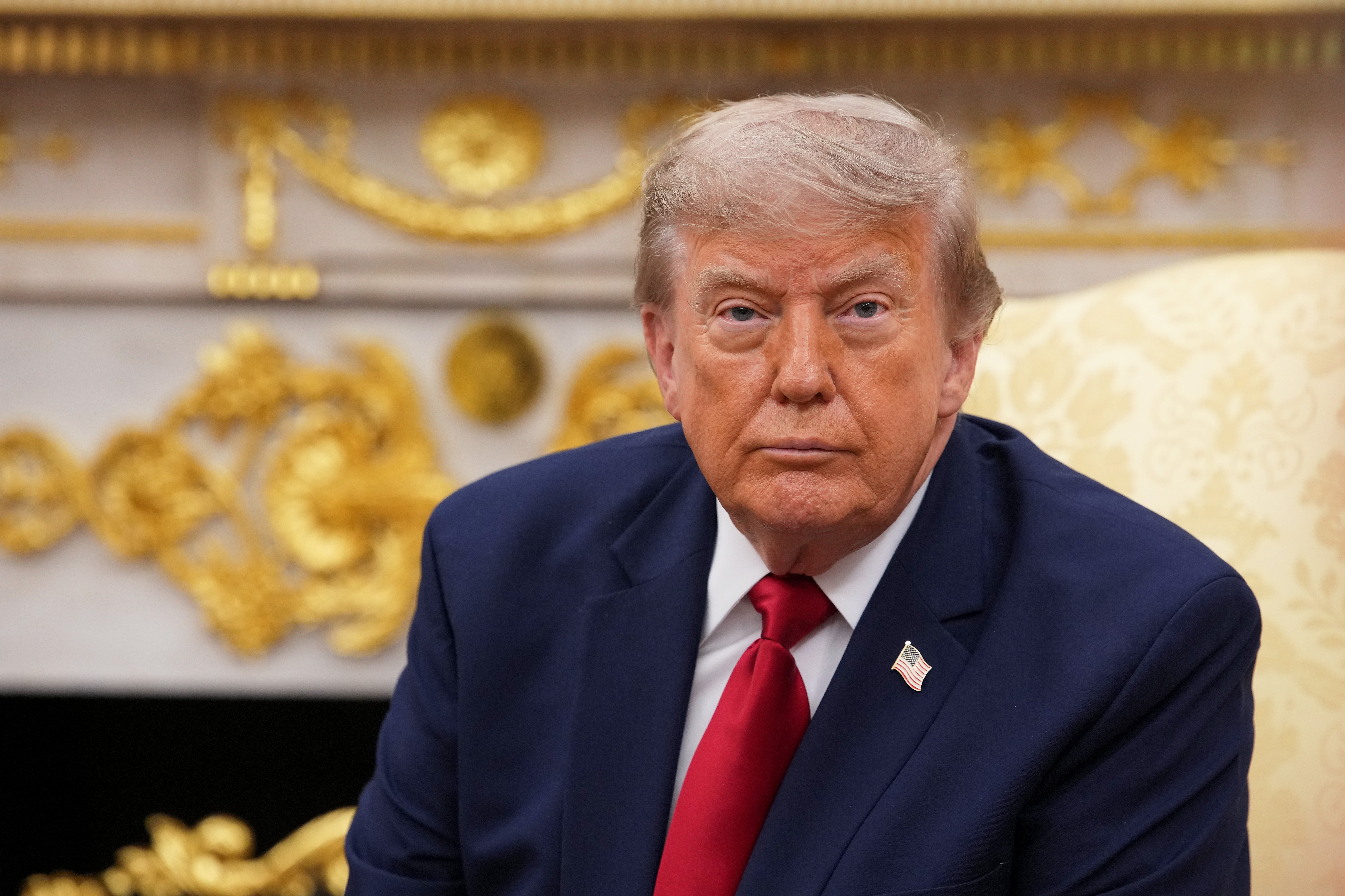 A idiosyncratic successful a suit and reddish necktie sits successful an ornate room, looking straight astatine the viewer