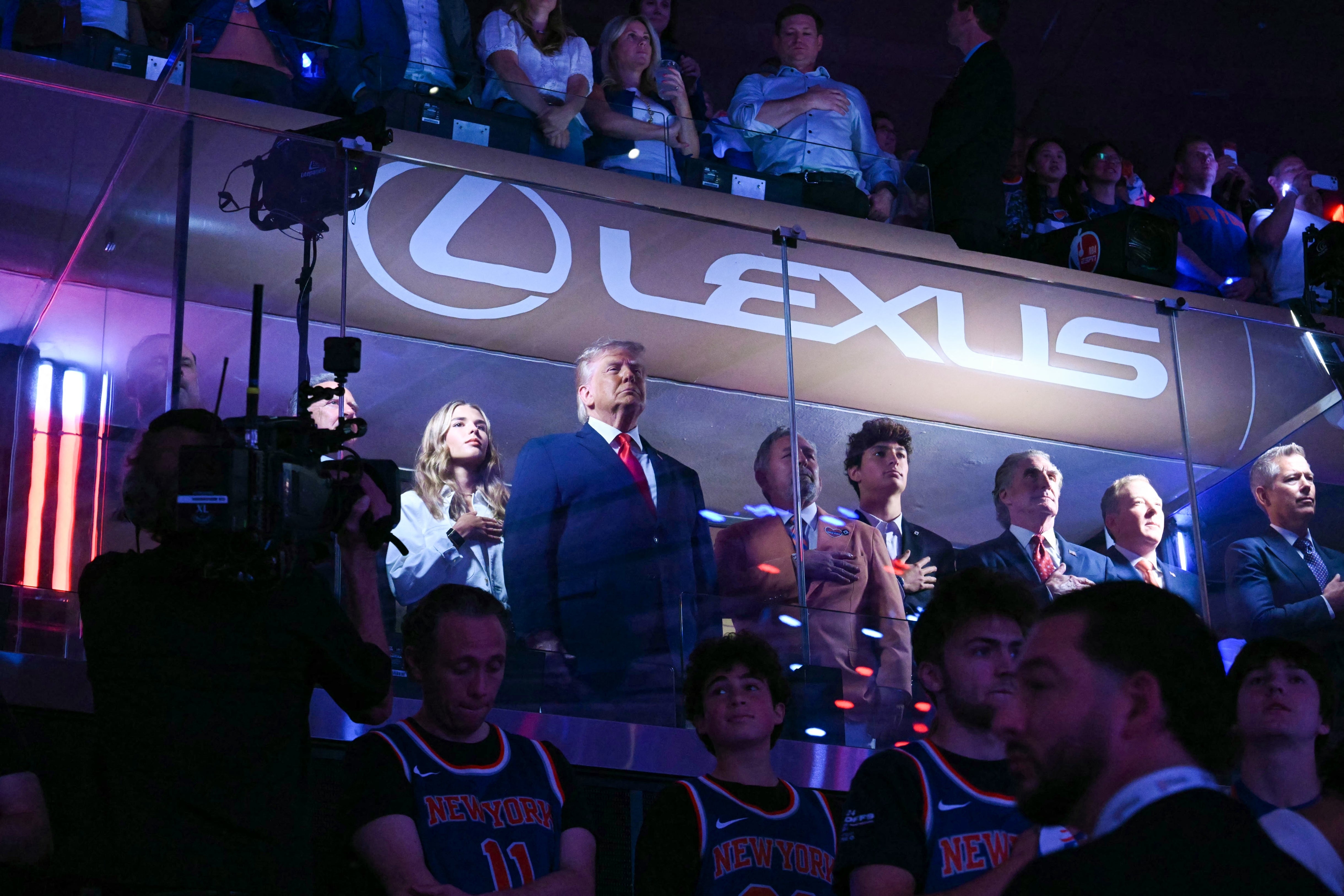 Group of people, including a notable fig successful a suit, basal successful a luxury sports container looking implicit a stadium crowd
