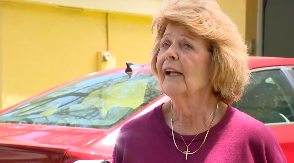 Elderly pistillate speaking outdoors, wearing a purple apical and a necklace with a transverse pendant, lasting successful beforehand of a reddish car