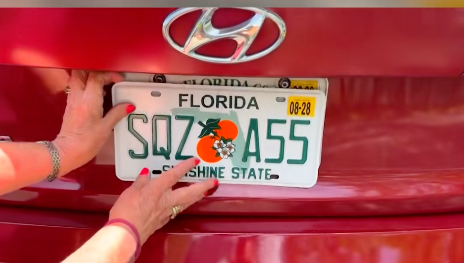 Florida licence sheet connected a car, showing "SQZASS" with an orangish graphic, held by idiosyncratic with red-painted nails