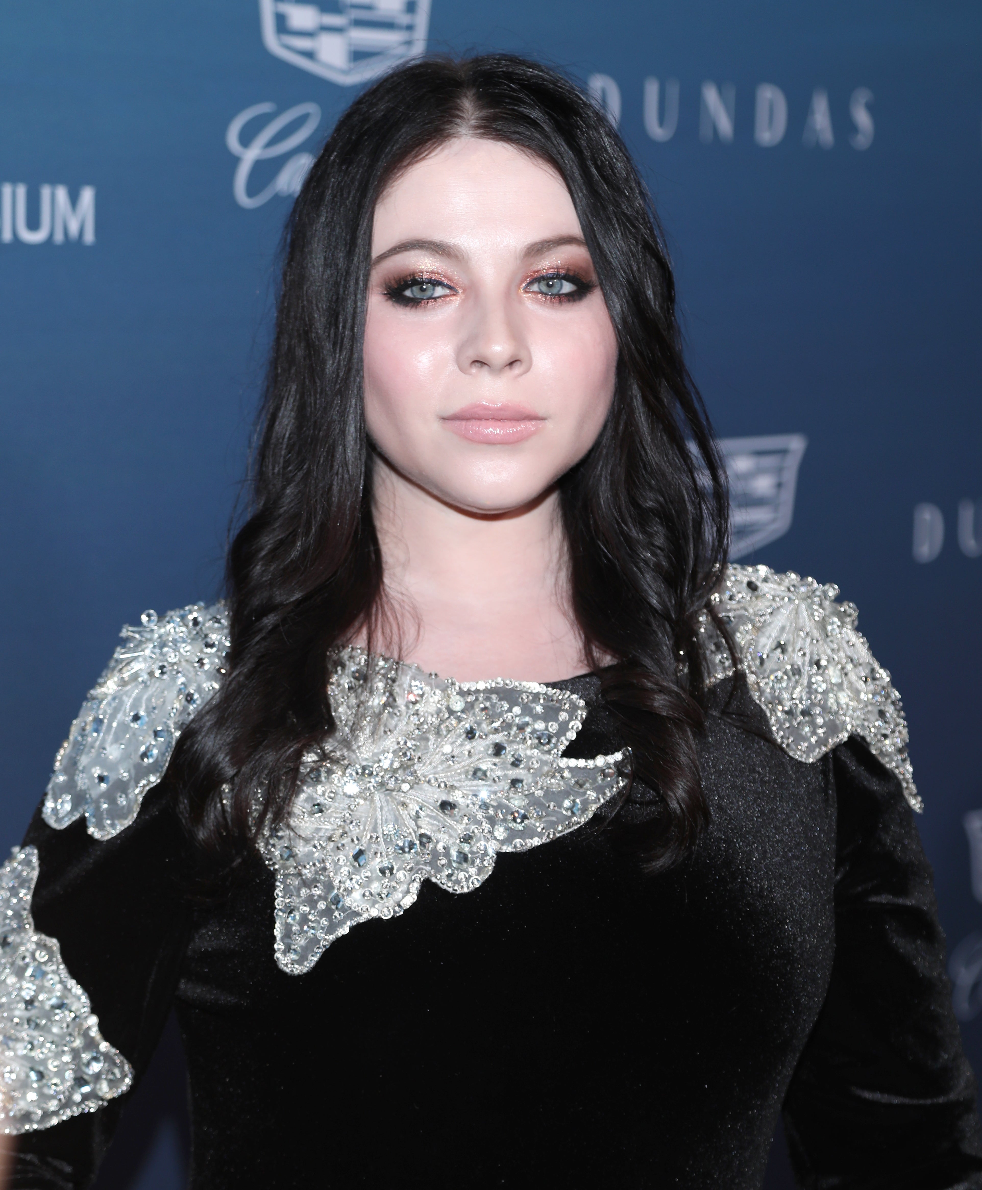 Michelle Trachtenberg in an elegant dress with intricate embellishments on her shoulders, posing at a celebrity event