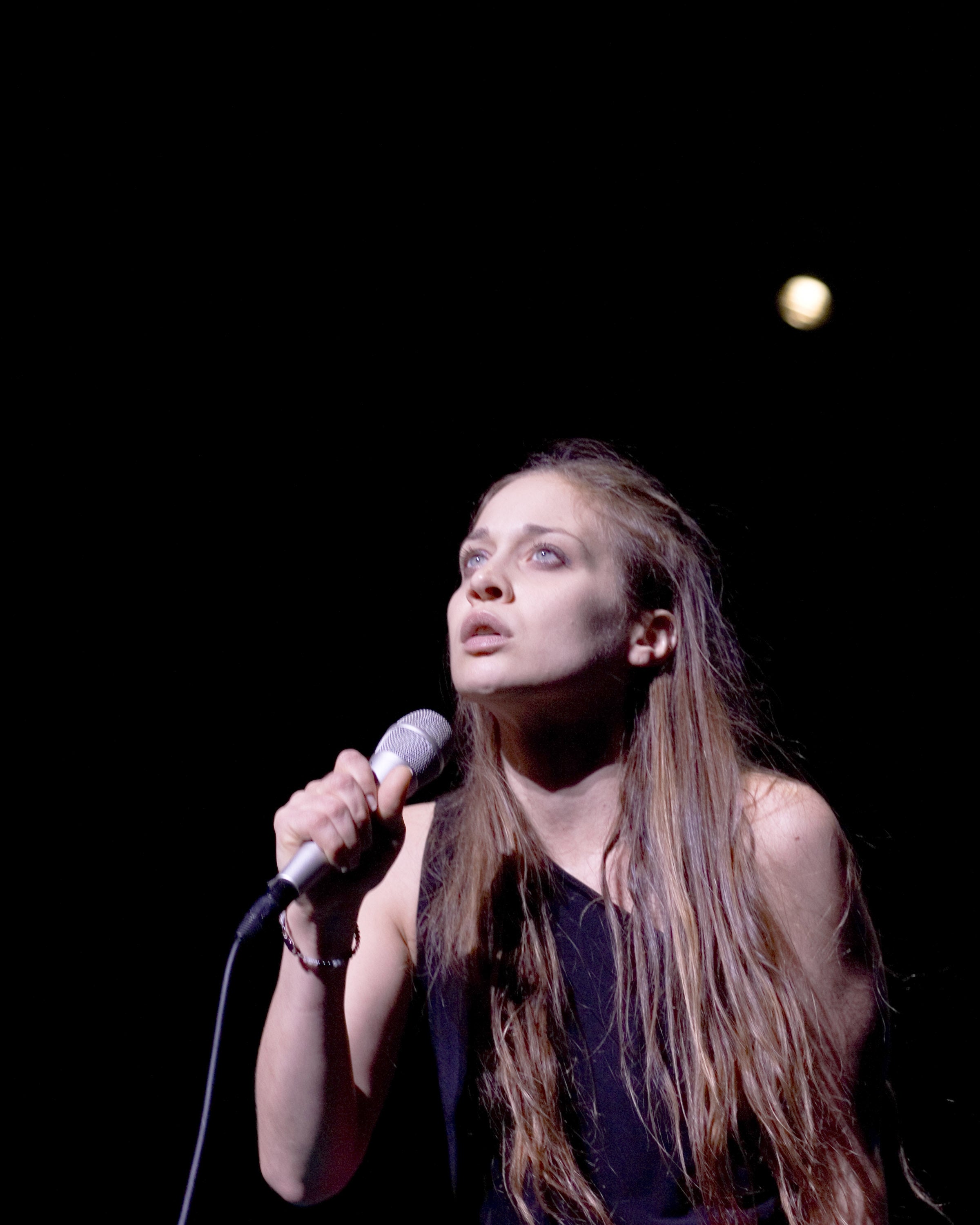 Fiona Apple connected  signifier    holding a microphone, looking upward with a focused expression