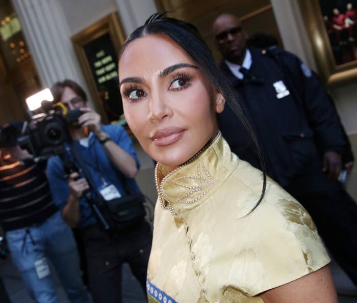 Kim Kardashian in elegant, high-collared dress posing for photos while security and media personnel are in the background