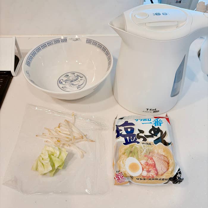 電気ケトル、ラーメンの包装、キャベツとモヤシ、ボウルが置かれているキッチンカウンター。