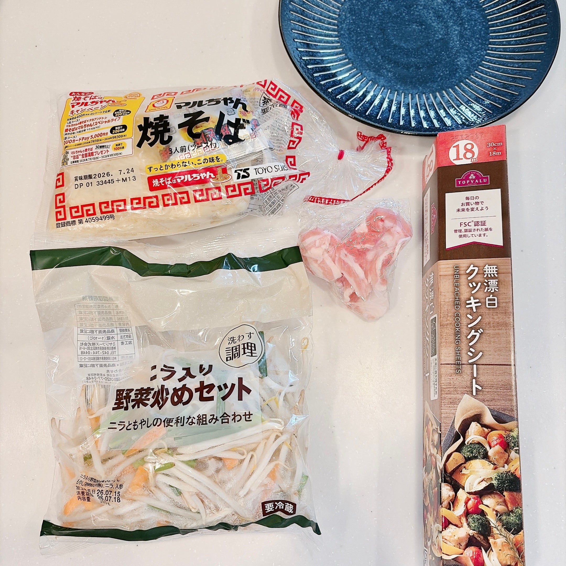 焼きそばの麺、カット野菜、豚肉、クッキングシートが置かれた、皿がキッチンカウンターののっている。