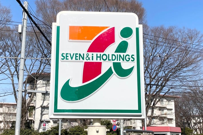 屋外にあるセブン＆アイ・ホールディングスの看板。背景は晴れた空と木々。