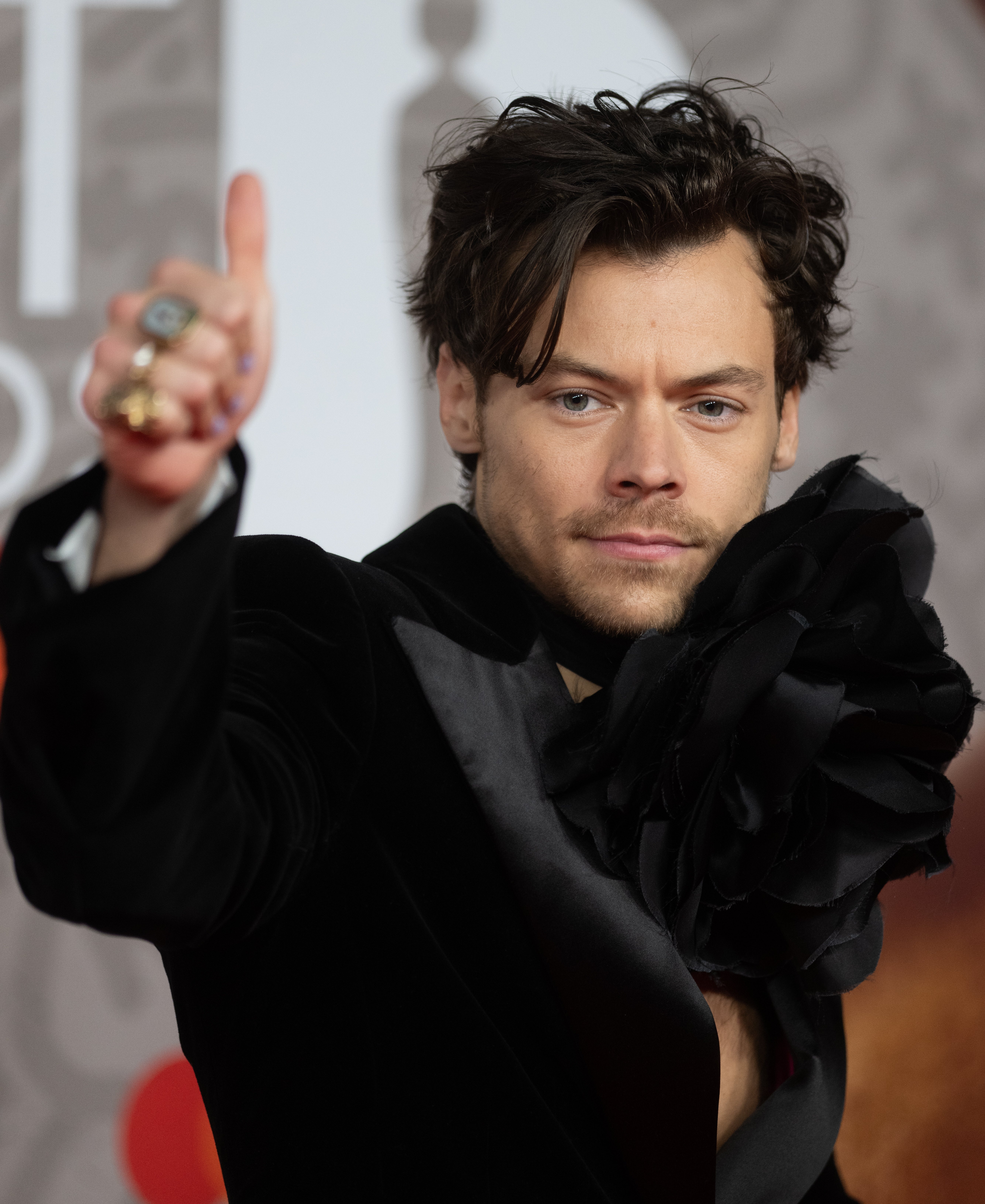 Harry Styles in a ruffled outfit poses with a thumbs-up gesture at a formal event