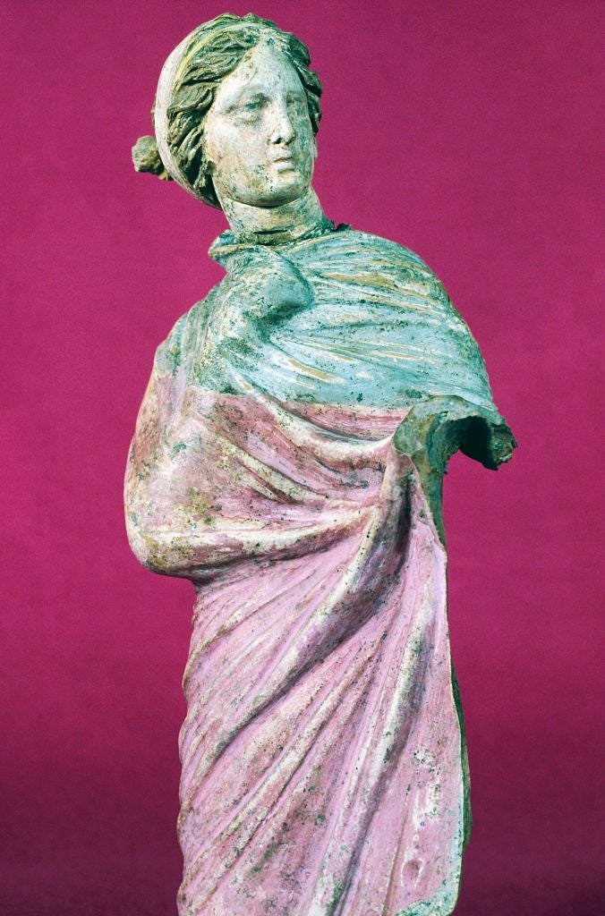 Ancient statue of a woman with a draped robe, missing arms, set against a plain background