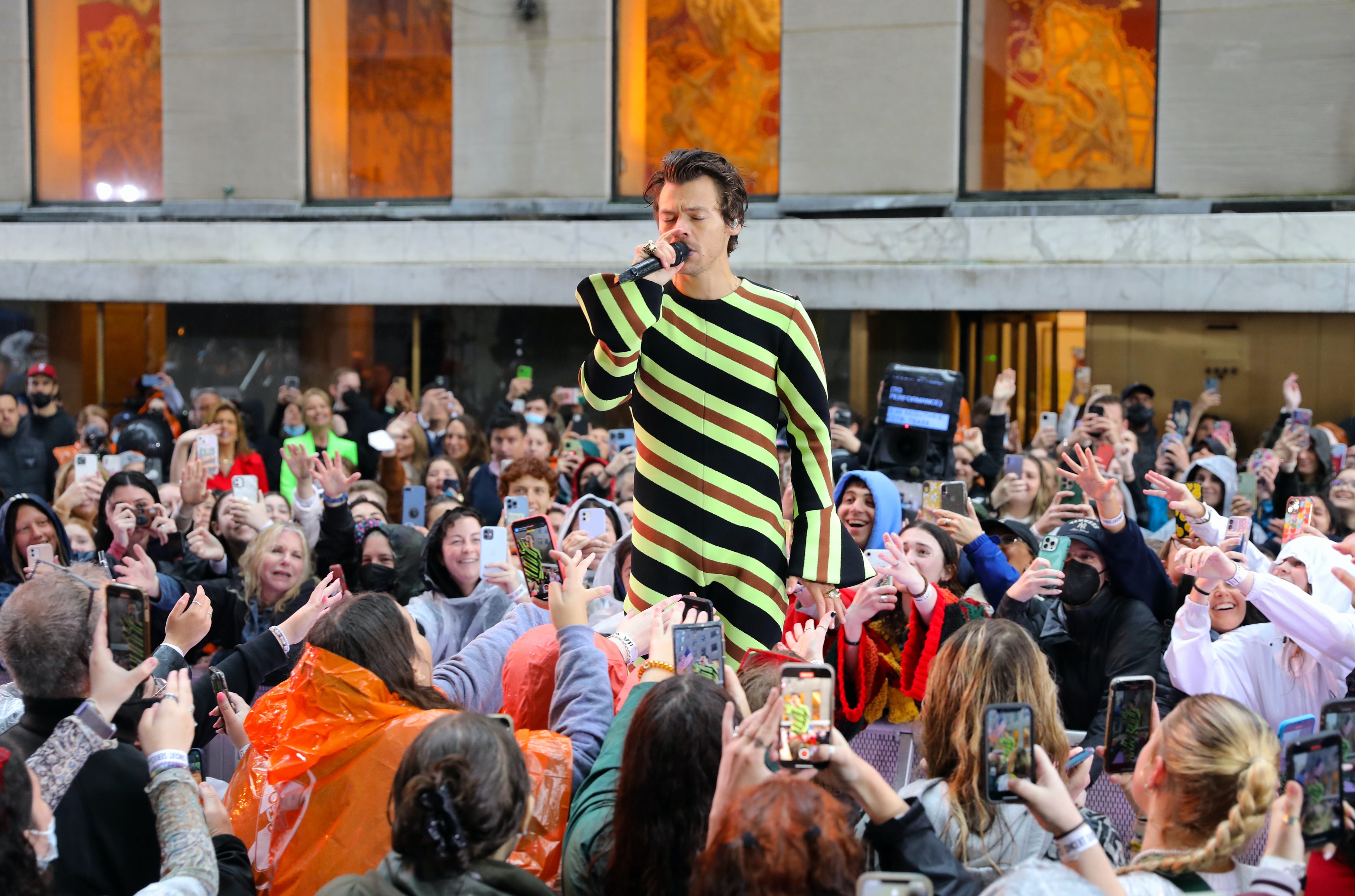 Harry Styles performs in a crowd wearing a bold striped outfit