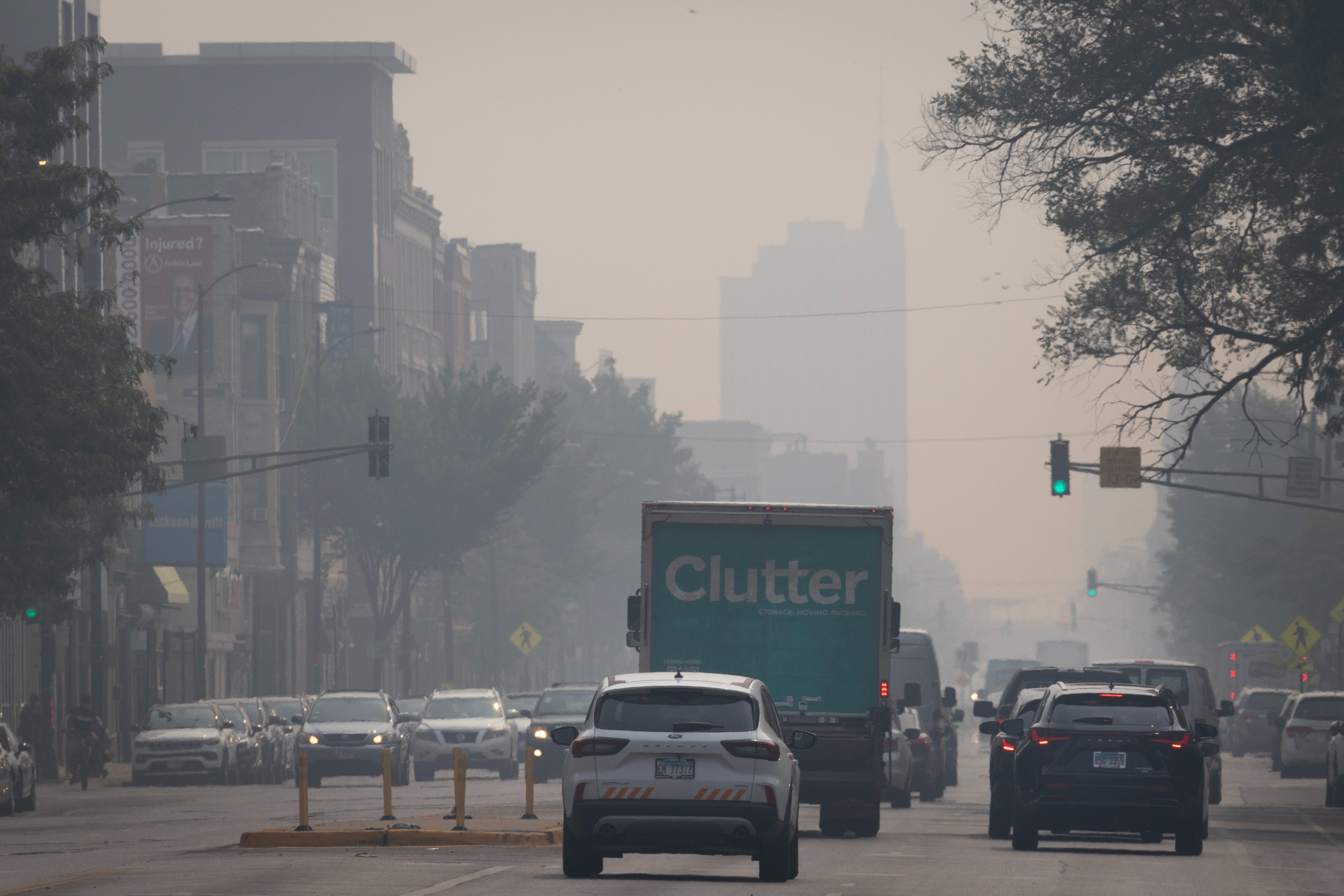 Bygate med tung smog eller tåke som skjuler bygninger i det fjerne. Biler og en lastebil i trafikken
