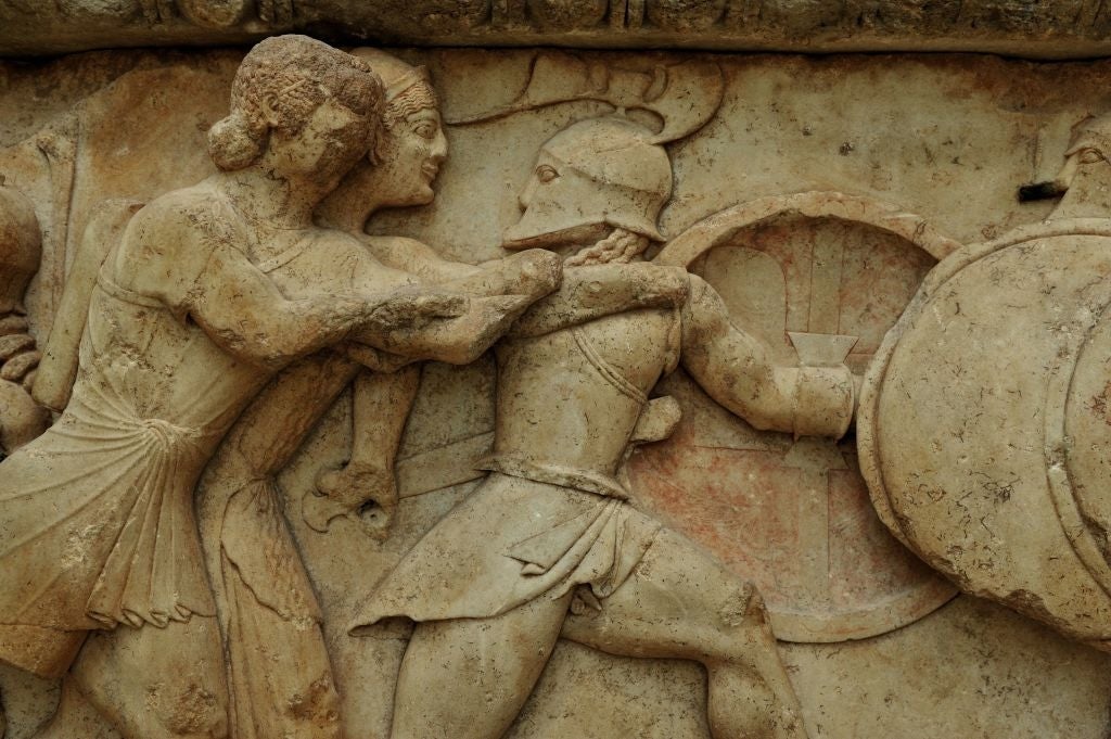 Ancient stone relief depicting two warriors in combat; one holding a shield, the other appears to be attacking with armor and helmet