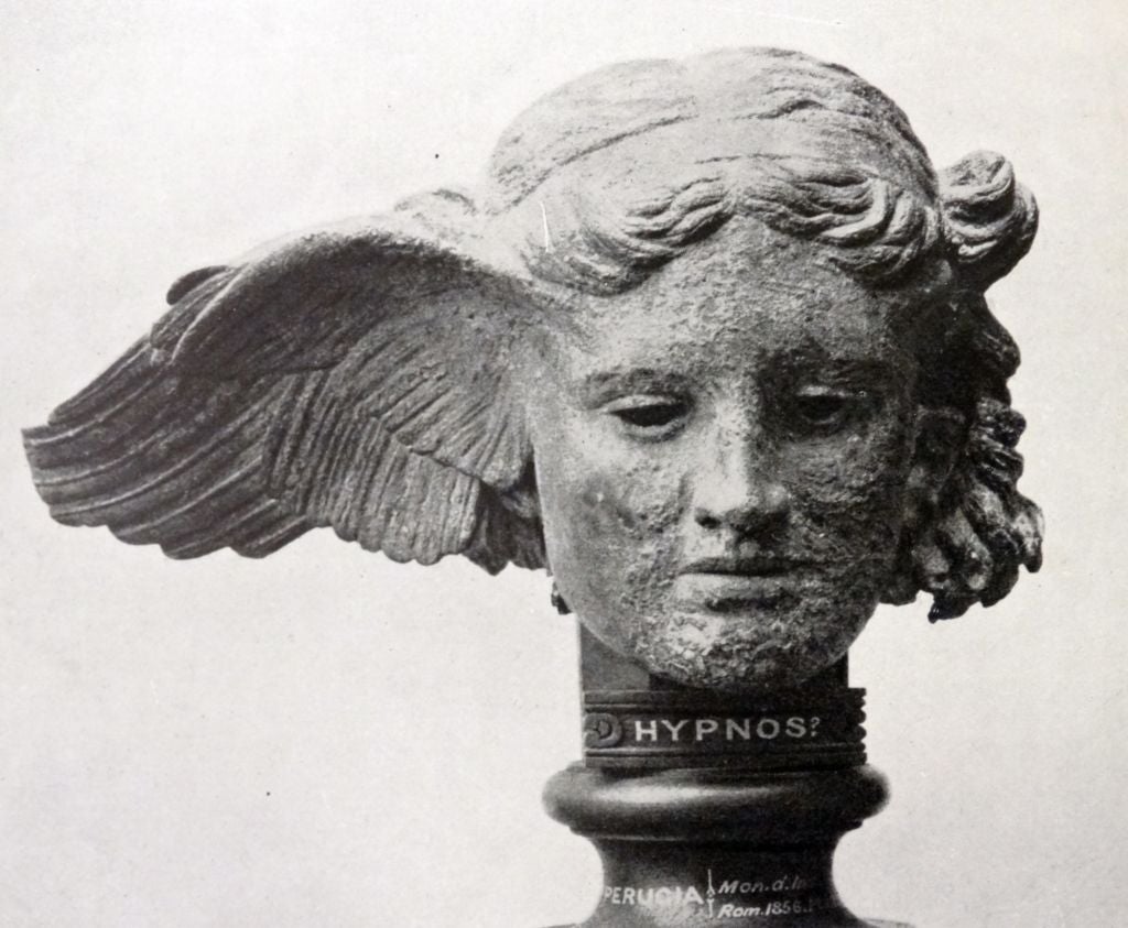 Stone sculpture of a winged head, possibly representing the Greek god Hypnos, mounted on a pedestal