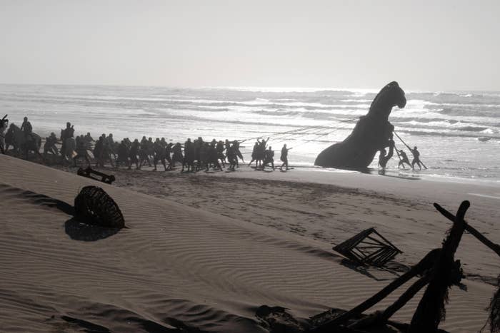 A large group of people pulling a massive ship's hull onto a beach, creating an epic and cinematic scene