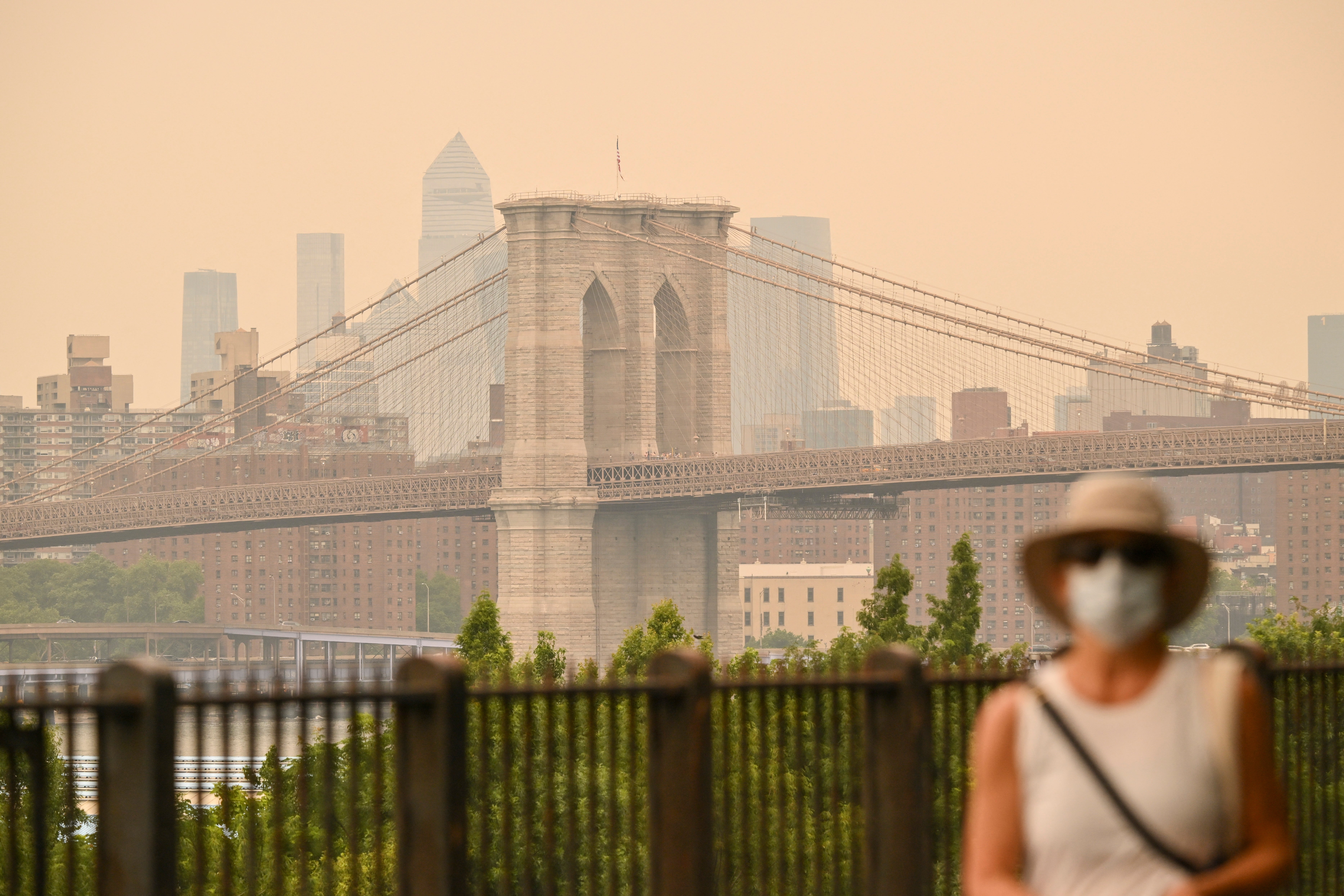 Brooklyn Bridge under disig himmel, person i forgrunnen med hatt og maske