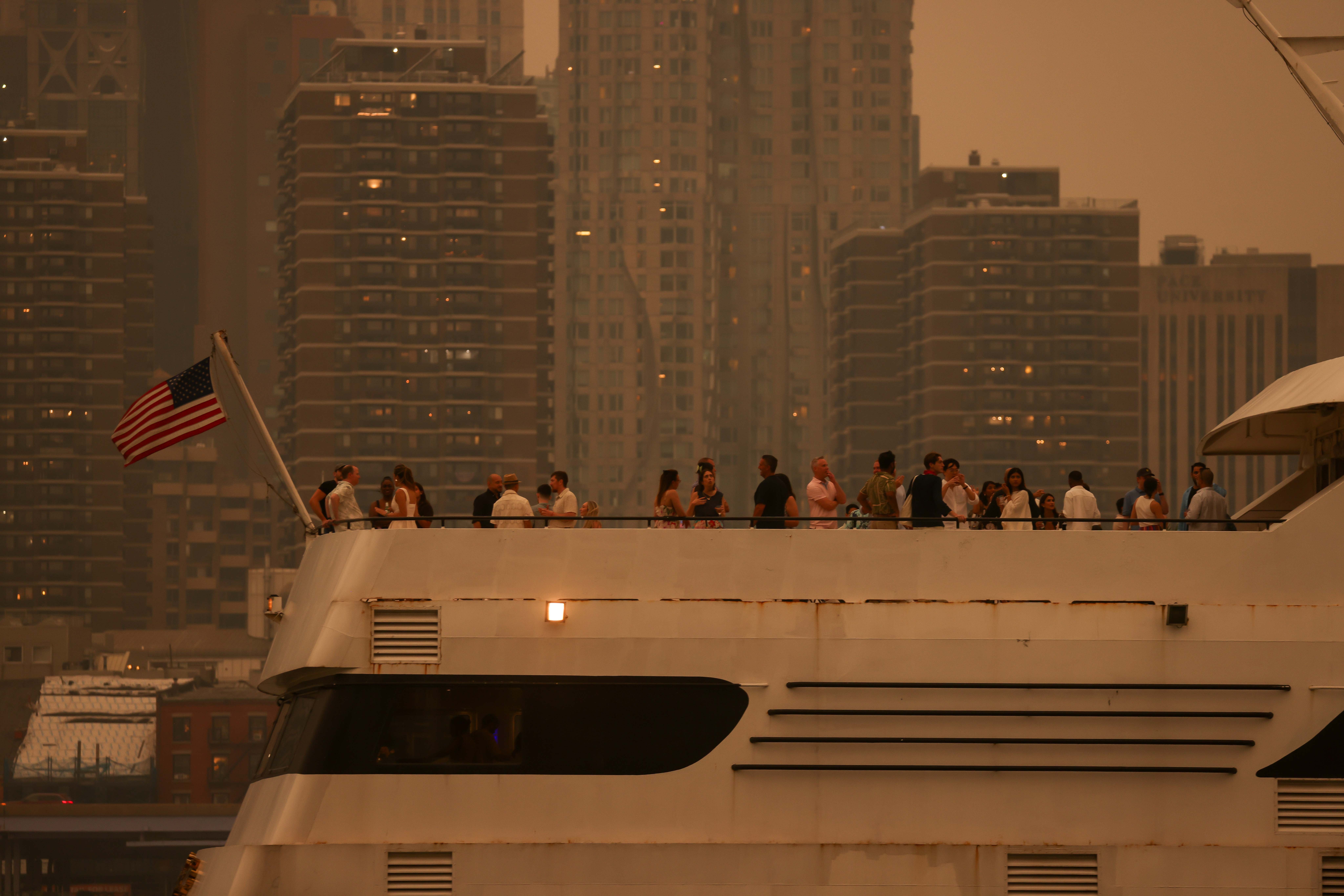 Folk på en luksusyacht i en urban havn, byens skyline i bakgrunnen, amerikansk flagg synlig