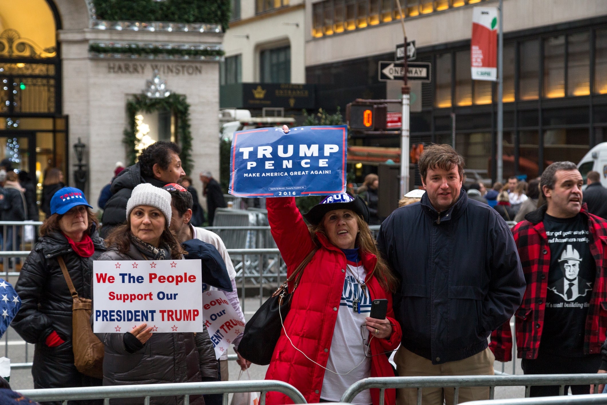 Folk som holder pro-Trump-skilt i en bygate, står bak metallbarrierer, omgitt av andre fotgjengere