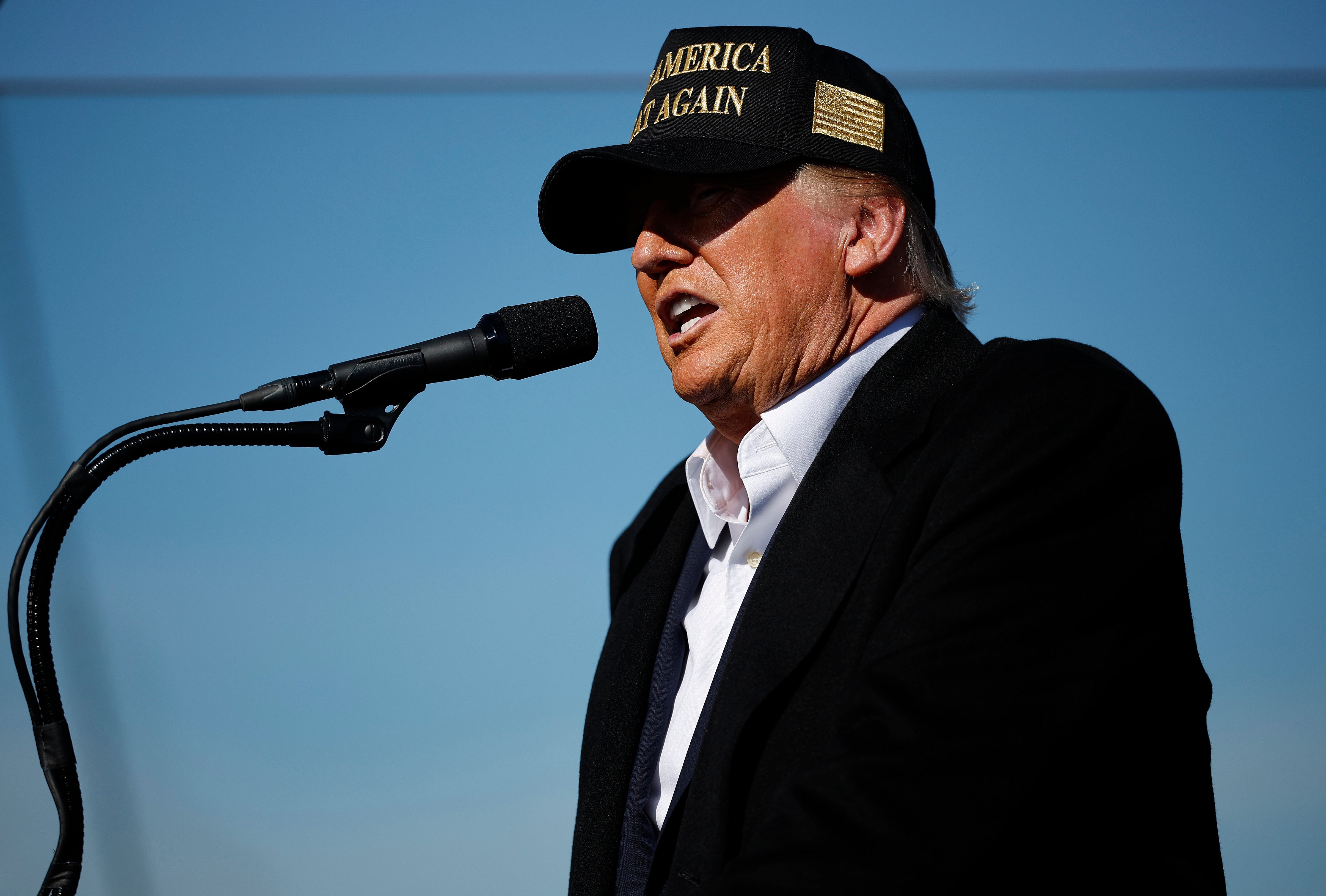 En person i en "Make America Great Again" cap snakker inn i en mikrofon på et utendørsarrangement