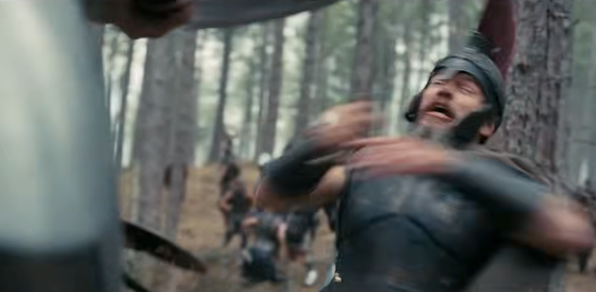 A scene from a historical movie featuring a helmeted warrior in armor appearing startled in a forest setting during battle