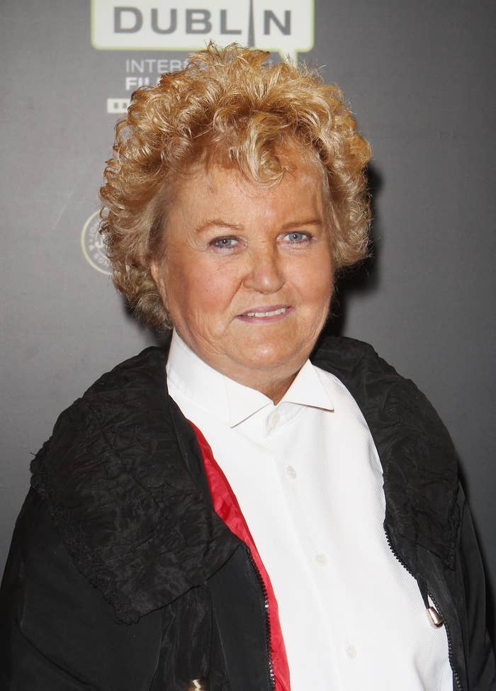 Person in a white shirt and dark jacket at an event; curly hairstyle