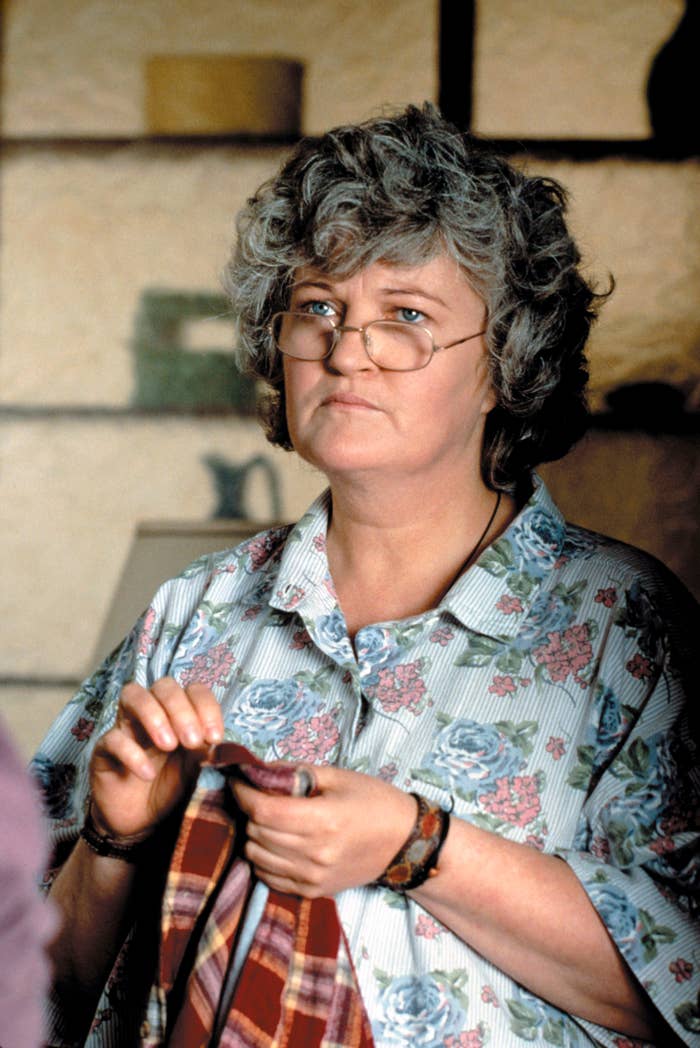 Person with curly hair and glasses wearing a floral blouse, holding fabric indoors