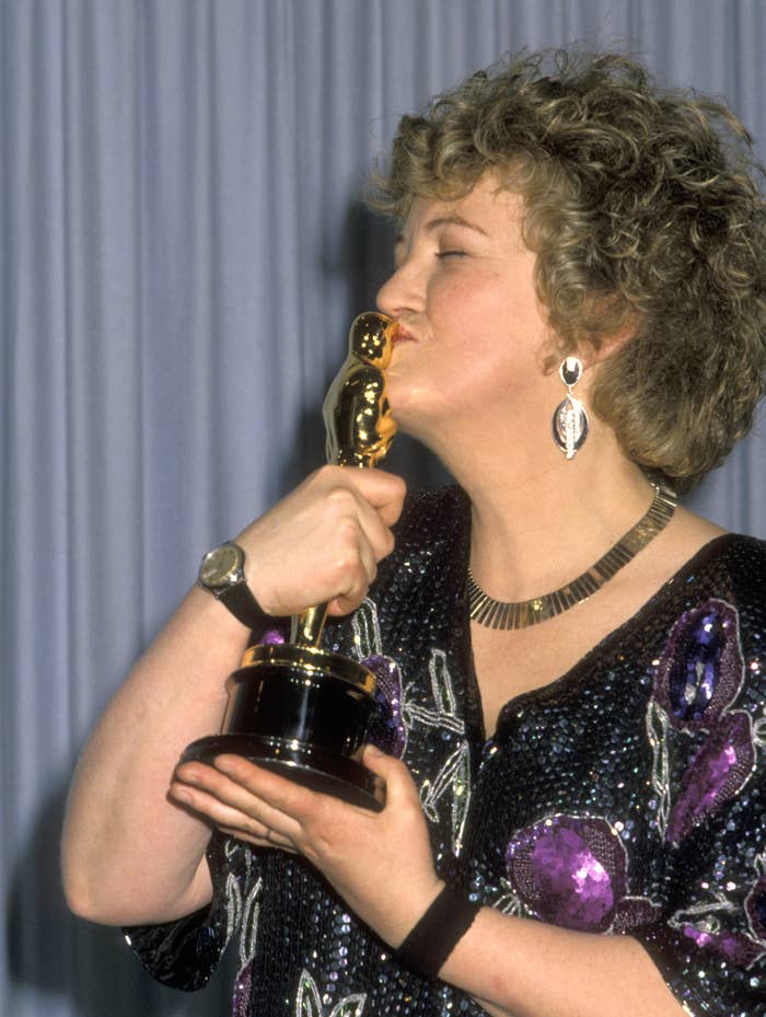 Person kissing an award statue, wearing a patterned outfit and large earrings, captured in a celebratory moment