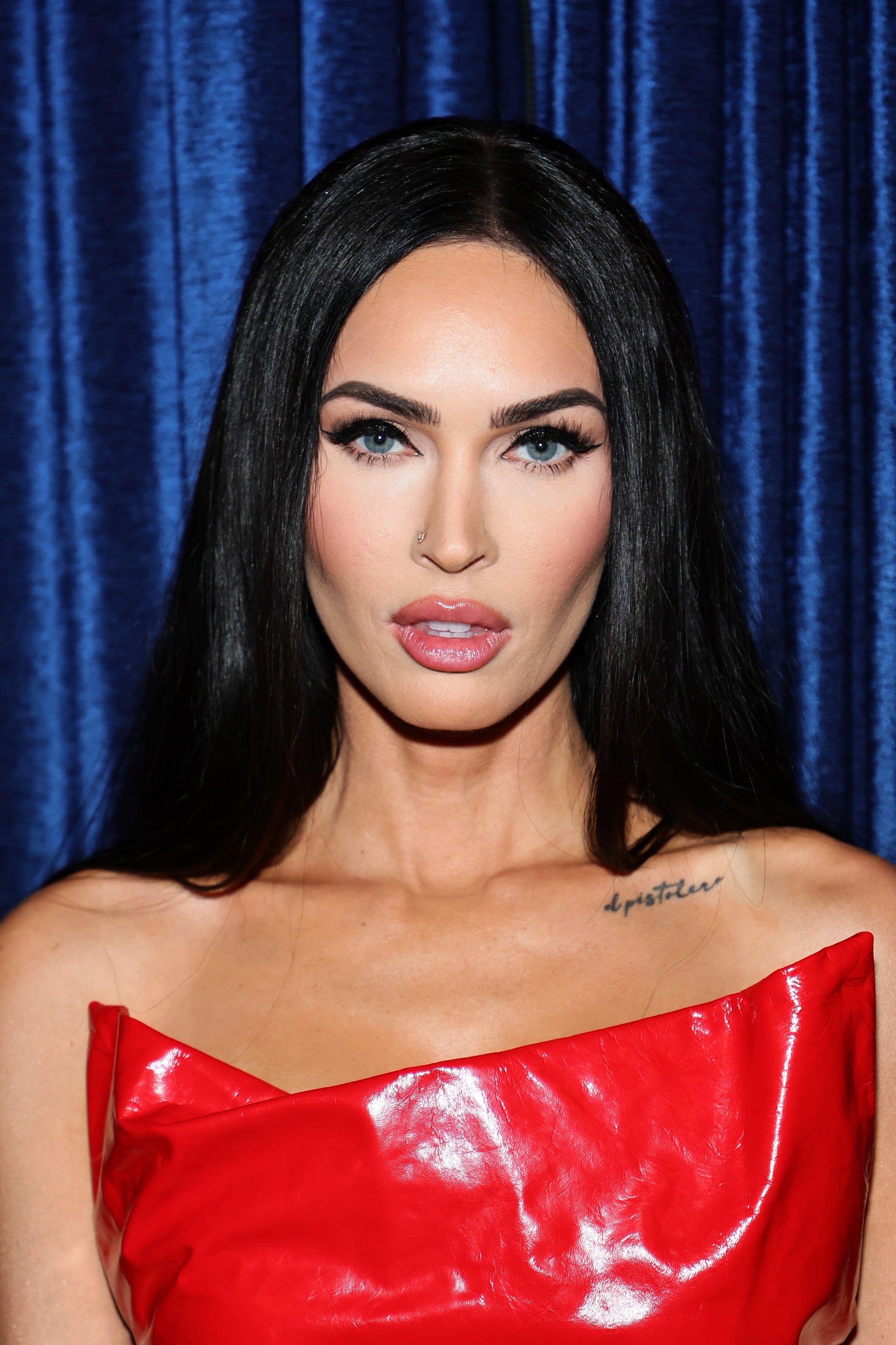 Megan Fox successful  a sleek reddish  strapless outfit poses against a curtain backdrop
