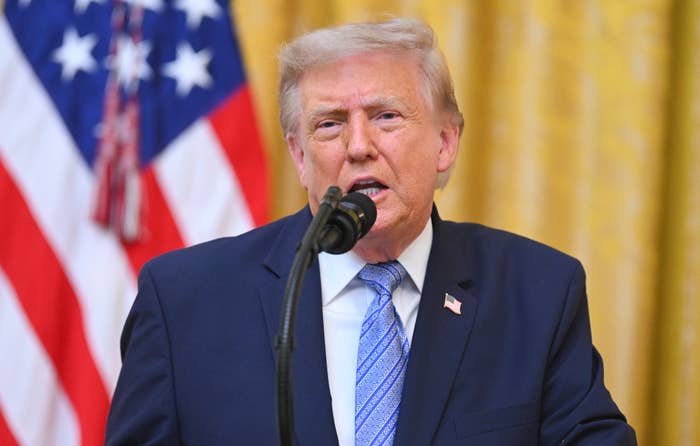 A antheral   successful  a suit   and bluish  necktie  speaks astatine  a podium with a microphone, lasting  successful  beforehand   of the U.S. flag