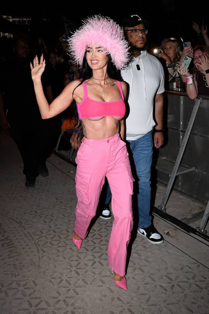 Megan Fox successful  a luffy hat, harvest  top, and pants walking and waving, surrounded by fans taking photos