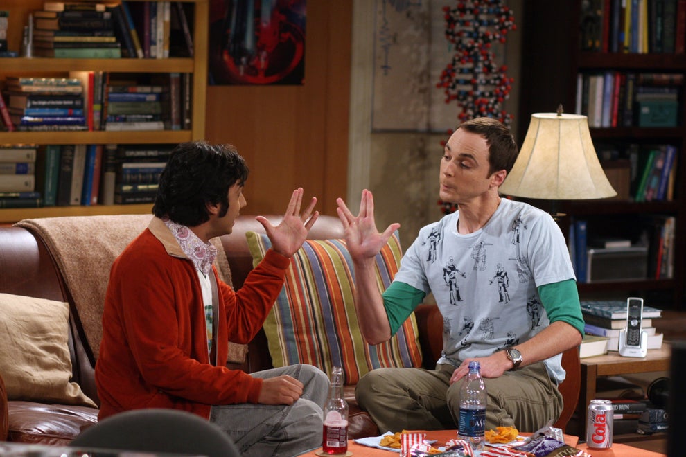 Two people sit on a couch doing a Vulcan salute from Star Trek, suggesting a humorous or nerdy context. Books and decorations are in the background
