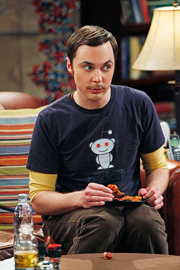 Person sitting on a couch, wearing a Reddit logo t-shirt, holding a plate with chicken wings