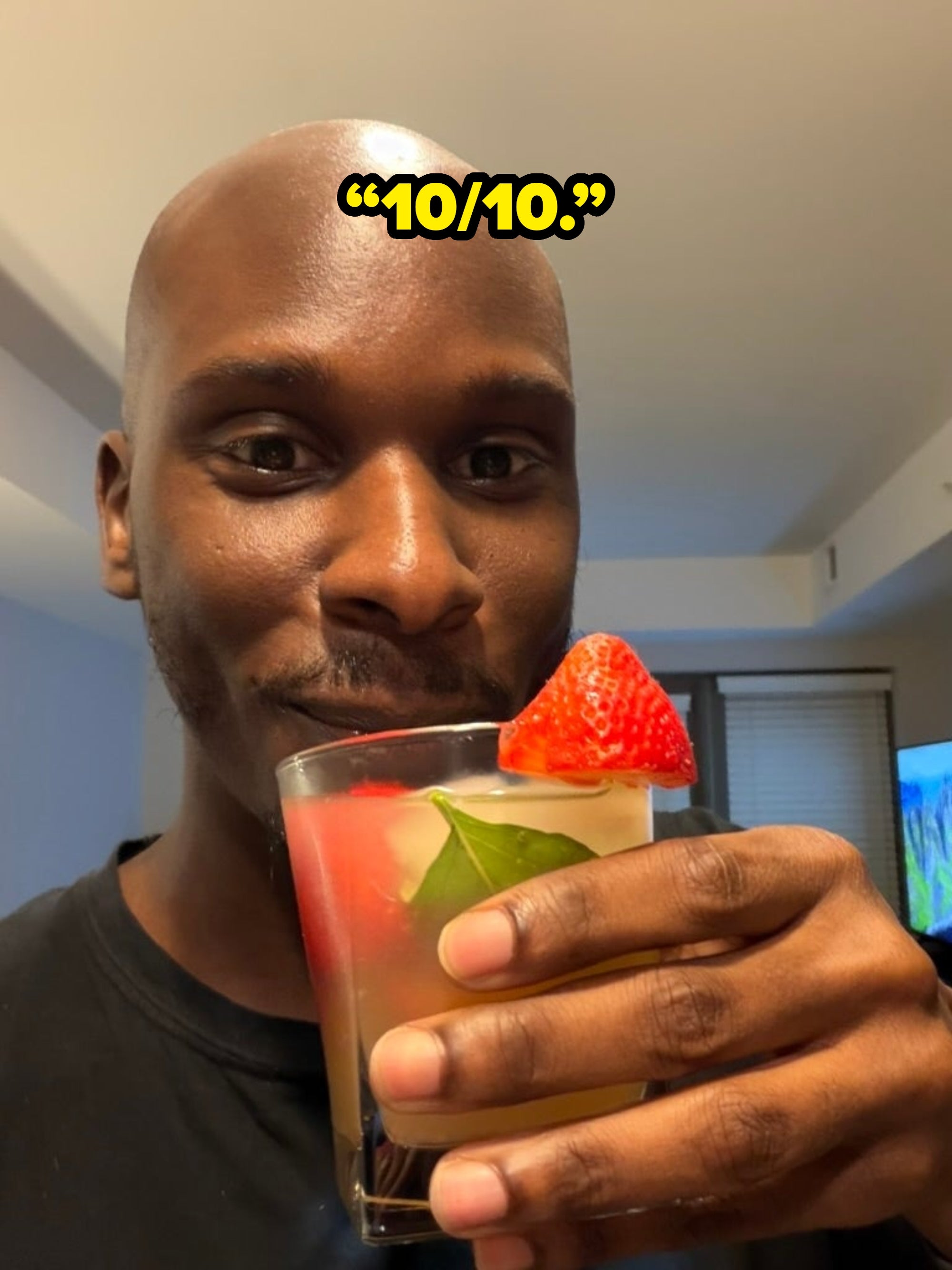 Person enjoying a cocktail in a glass with a strawberry and leaf garnish indoors