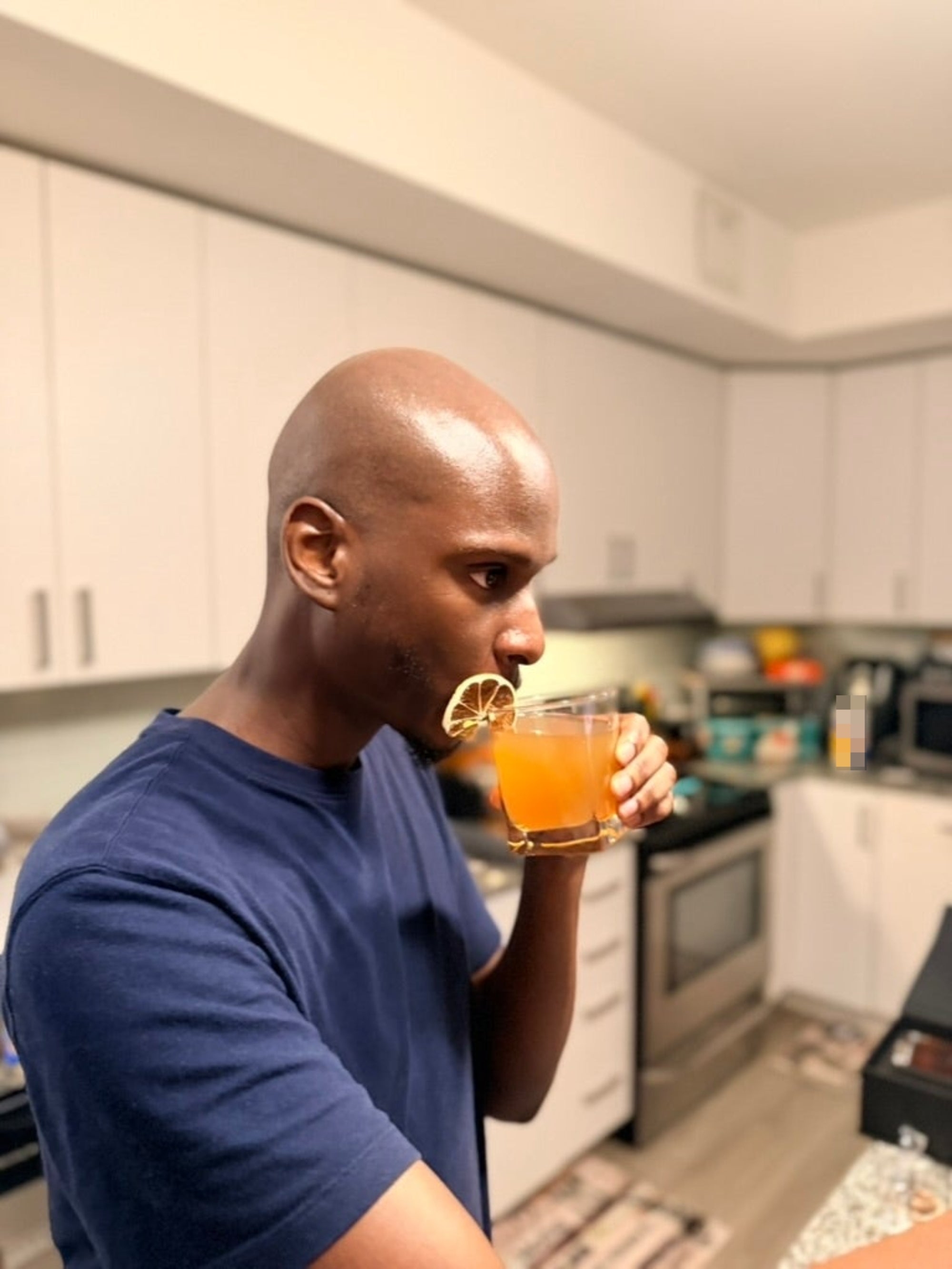 Person in a kitchen sipping a drink with a lime slice garnish
