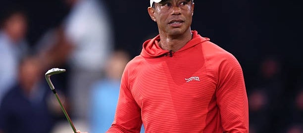 Person wearing a sporty outfit holds a golf club, looking focused, against an out-of-focus background