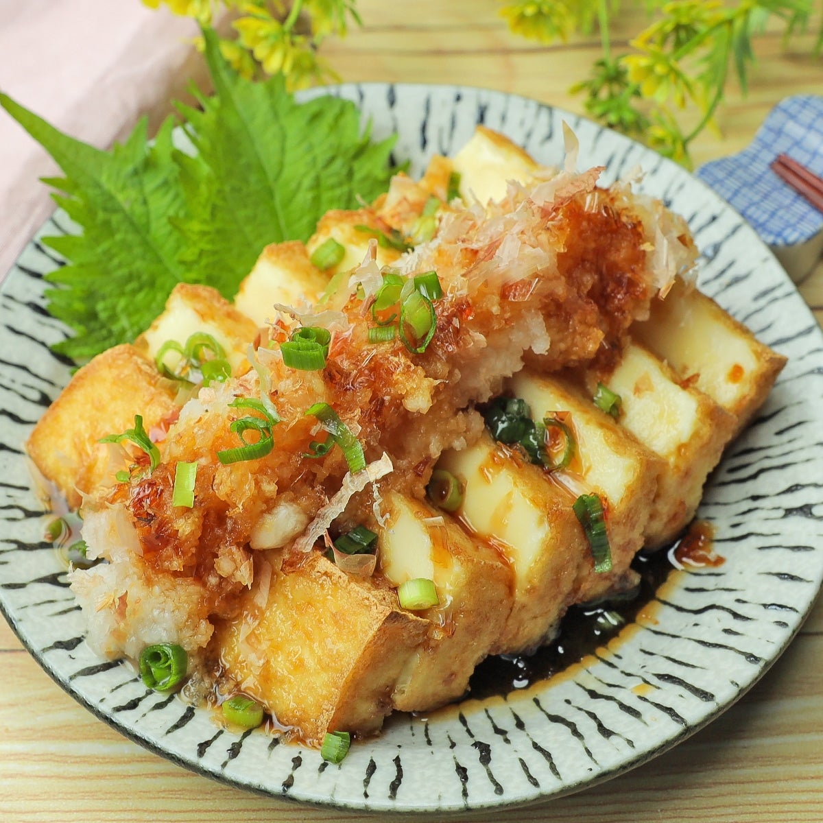 皿に盛られた厚揚げ料理、上には刻みネギとかつお節、大根おろしが載っている。