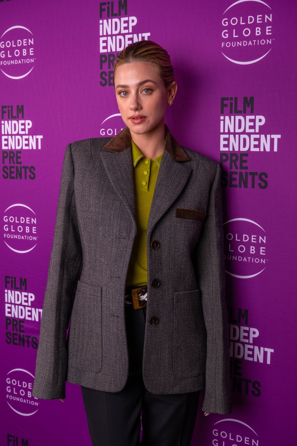 Lili Reinhart in a tailored blazer and polo stands in front of a backdrop with "Film Independent Presents" and "Golden Globe Foundation" logos