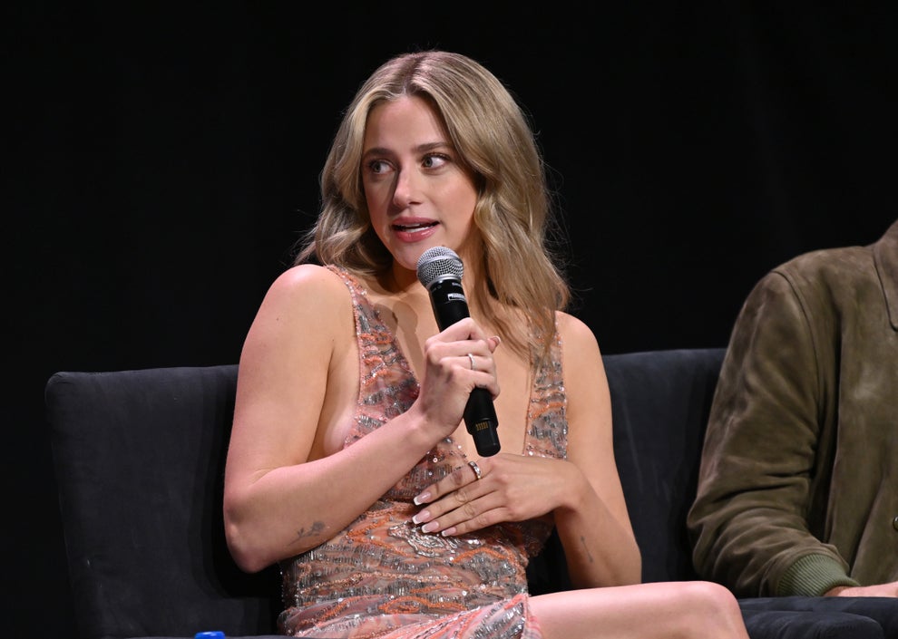 Lili Reinhart in an elegant, sparkling dress speaks into a microphone while seated on a panel