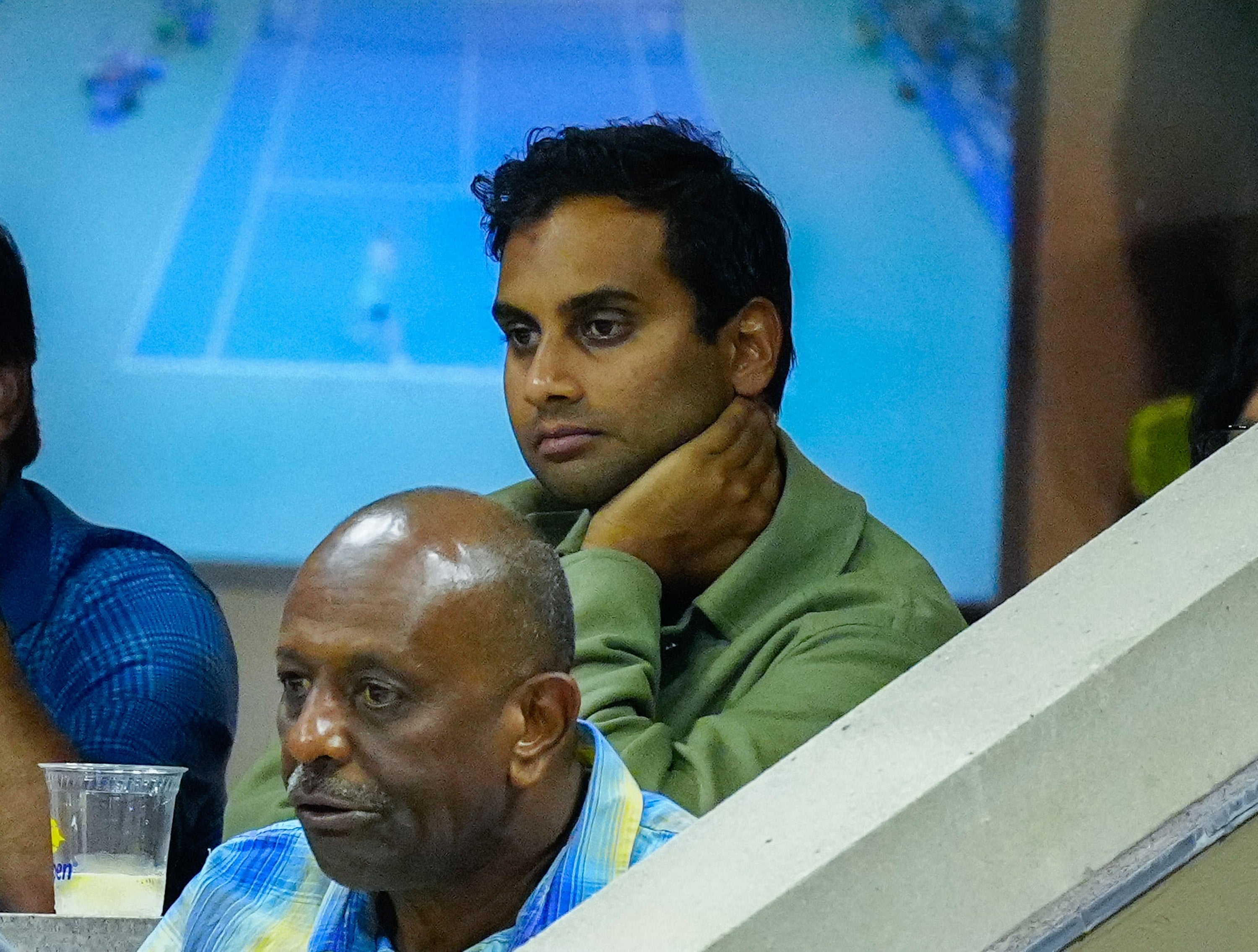 Aziz Ansari sits in the audience at a sports event, attentively watching