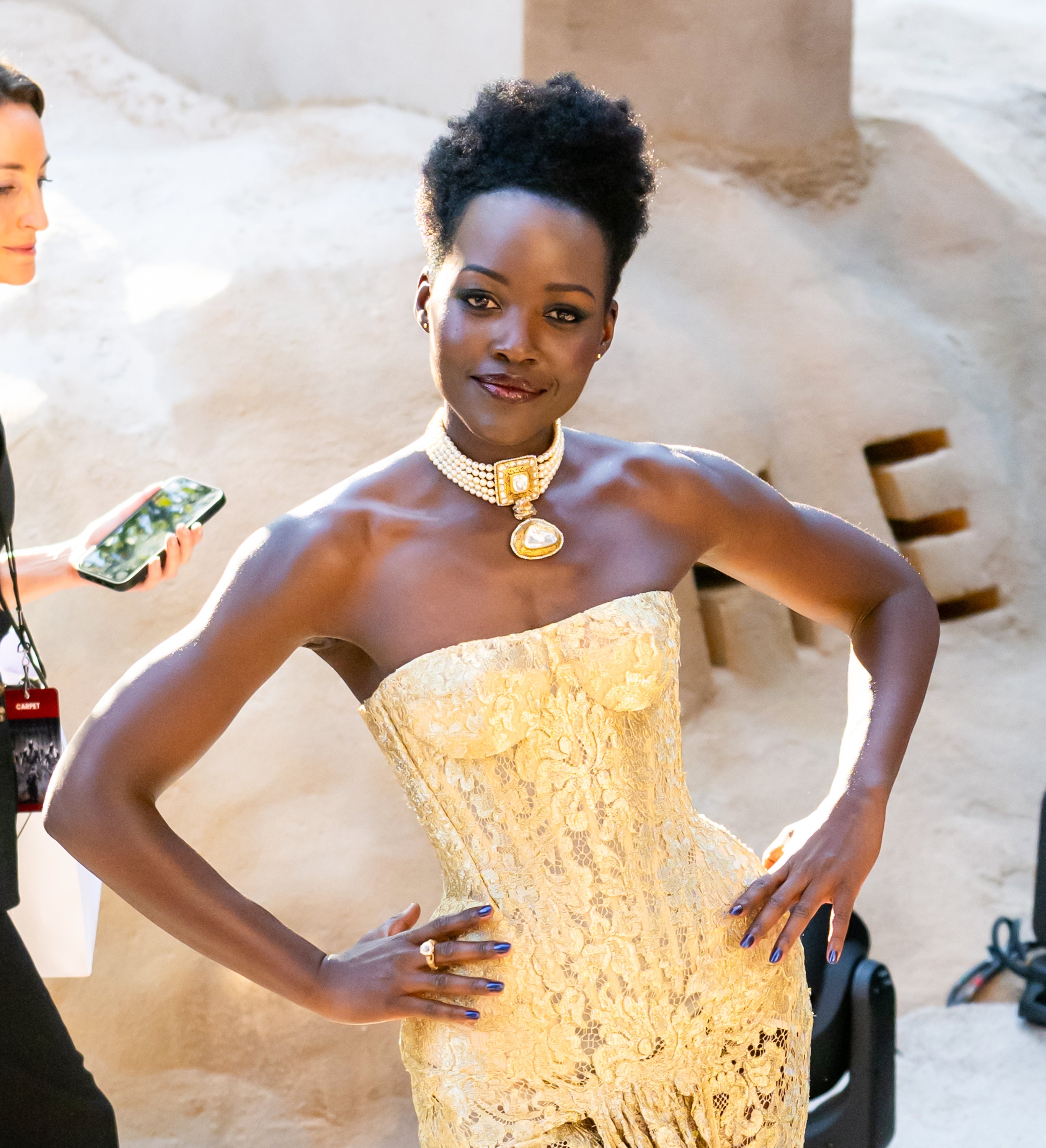 Woman in a strapless, textured gown with statement jewelry poses confidently at an event