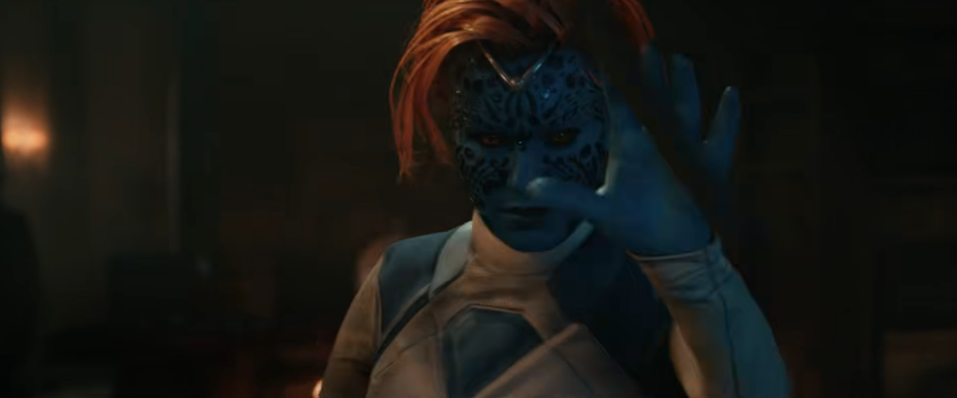 A character in a sci-fi film with intricate facial markings and vivid distinct skin raises their hand dramatically in a dimly lit setting