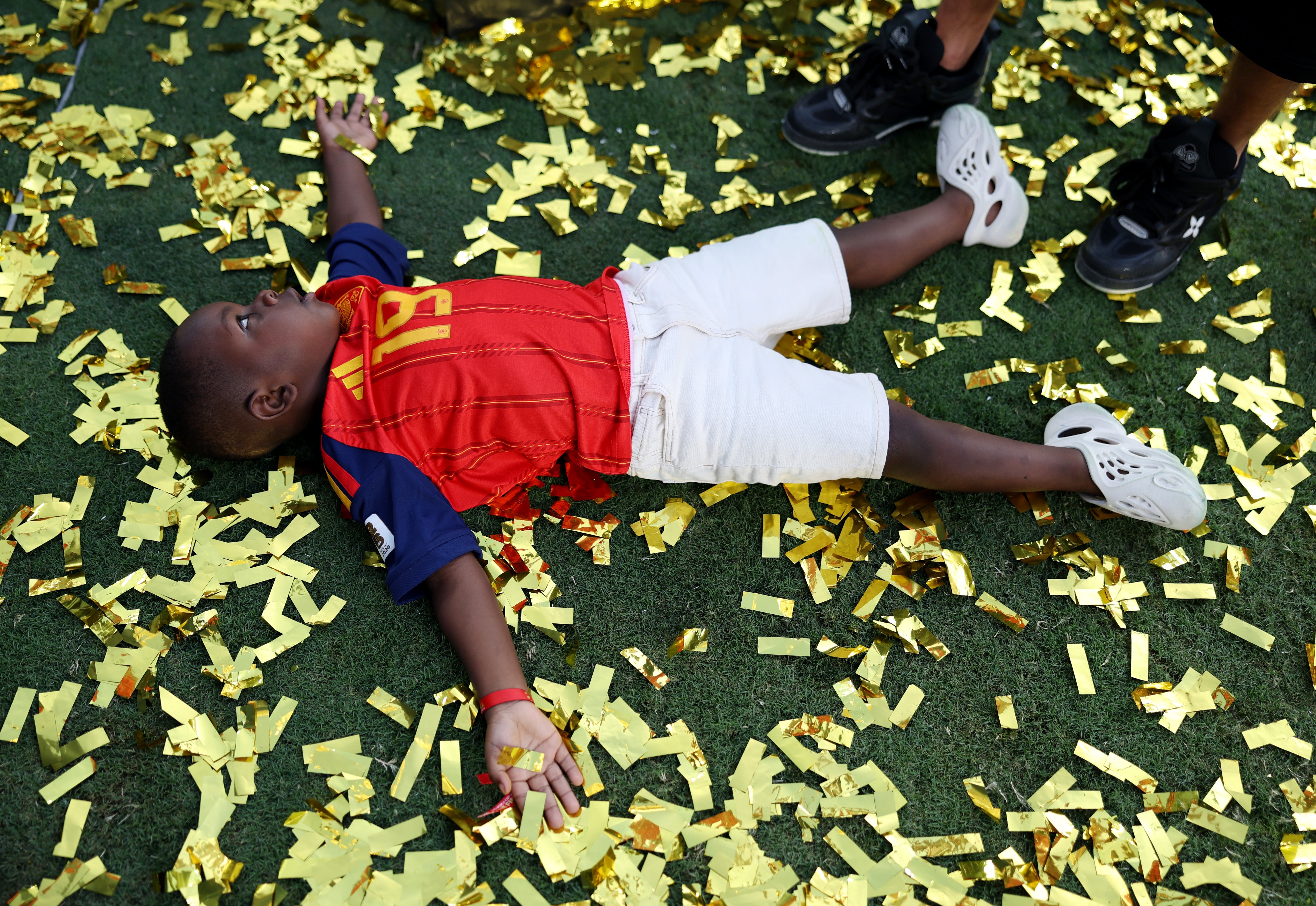 Child joyfully lying connected writer among golden confetti, wearing a sports jersey and achromatic shorts, with radical lasting nearby
