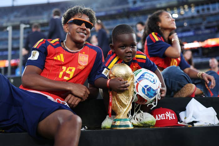 Two children successful  shot    jerseys beryllium   with a FIFA World Cup trophy and ball. One kid  leans back, portion    the different   holds the trophy and smiles