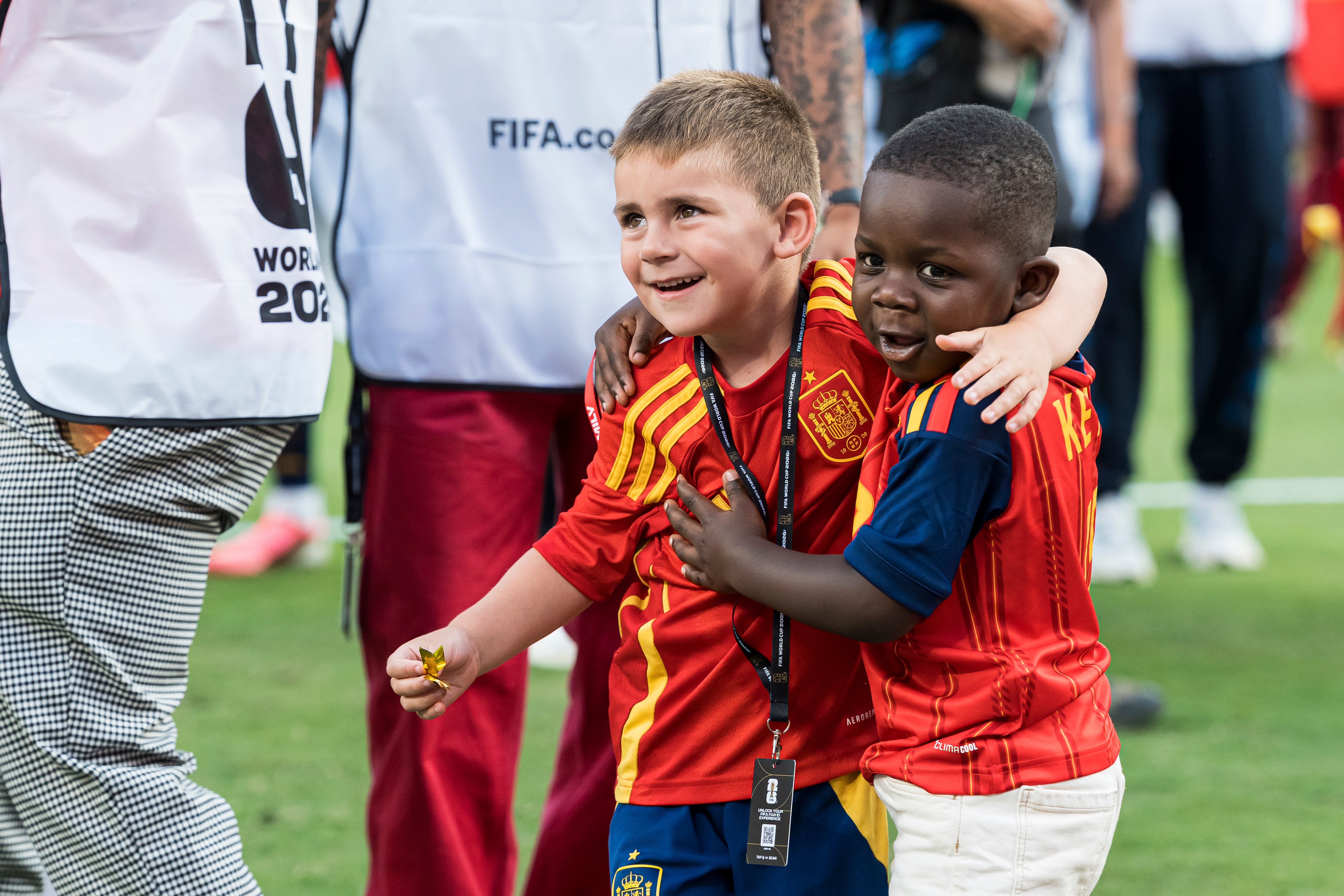 Two young children connected a sports field, some successful akin shot jerseys, smiling and hugging. People astir them look to beryllium portion of an lawsuit staff